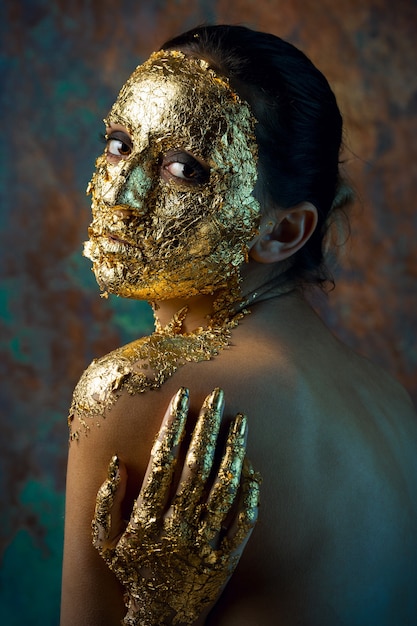 Girl with a mask on her face made of gold leaf Gloomy studio portrait of a brunette