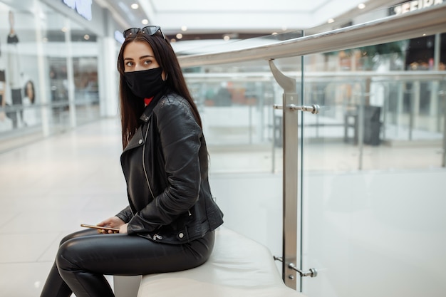 Girl with a medical black mask and mobile phone in a shopping center