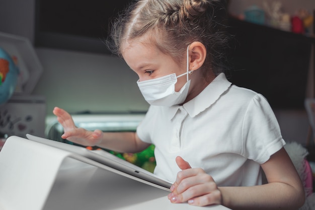 Girl with medical mask on her face concentrated on her task with tablet