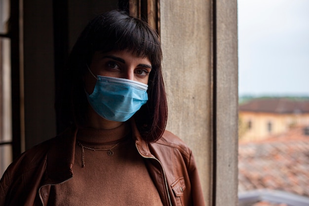 Photo girl with medical mask at window in her home during covid quarantine period