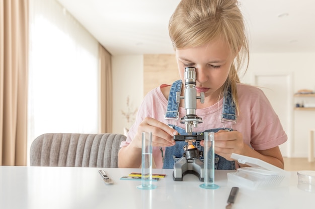 Ragazza con il microscopio a casa che impara chimica e gioco