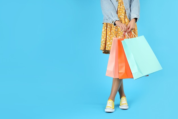 Girl with multicolored paper bags on blue background, space for text.