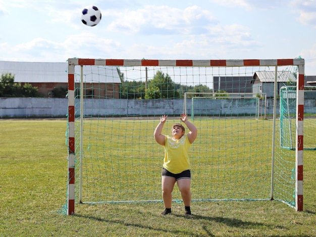 太りすぎの女の子がサッカーのゲートに立って、彼の手でボールをキャッチしたい