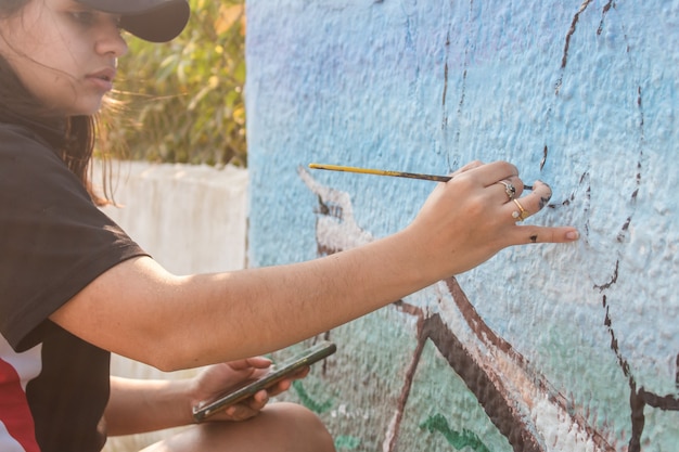 Girl with paint stains painting a street wall.