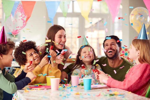 Photo girl with parents and friends at home celebrating birthday firing confetti poppers at party