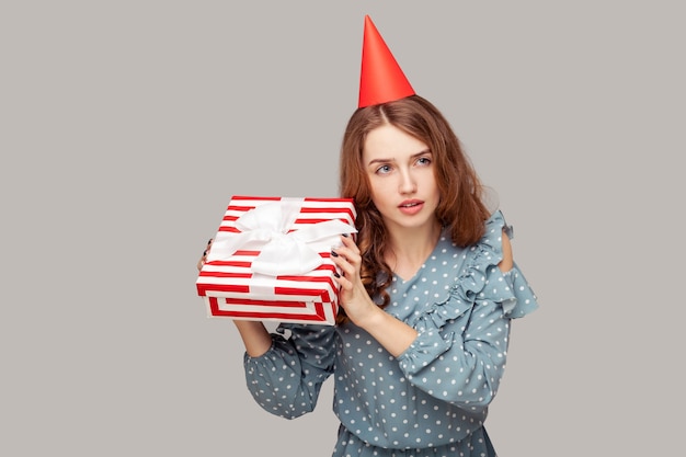 Girl with party hat holding gift listening to box, curious what bonus inside, celebrating birthday