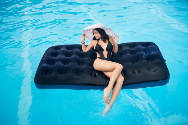 Girl with perfect figure lying on mattress in swimming pool