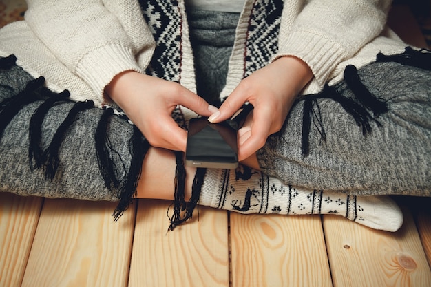 Girl with a phone in her hands sitting on the wooden floor.