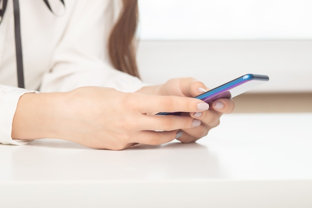 Girl with a phone at a table typing text on the screen