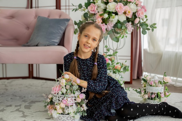 a girl with pigtails is sitting near a pink sofa with a basket of flowers in her hands