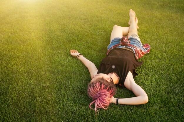 Photo girl with pink dreadlocks dreaming on the grass full of sunshine . freedom and dreams outdoors concept