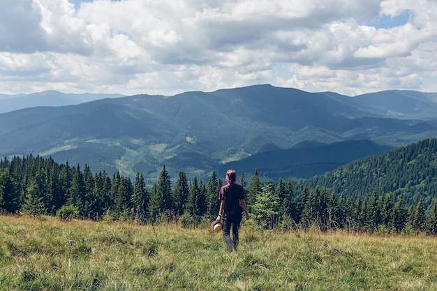 Girl with pink hair Standing on the clearing and looks at the mountains. Hiking through forest in summer. Dark autumn forest. Local Travel Concept.