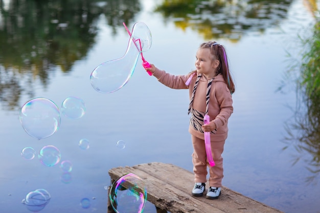 a girl with pink hair on a summer evening on a walk  lets soap bubbles on the water