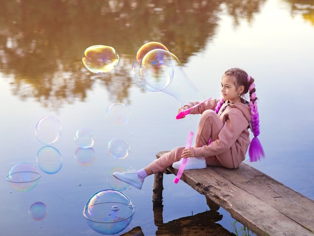 A girl with pink hair on a summer evening on a walk  lets soap bubbles on the water