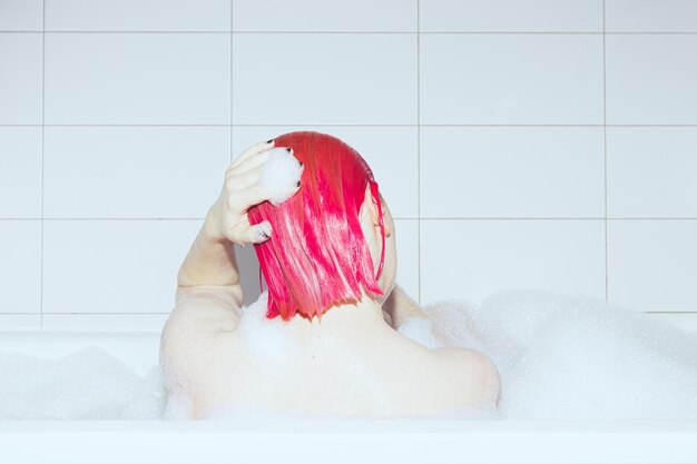 Girl with pink hair takes a bubble bath self care back view