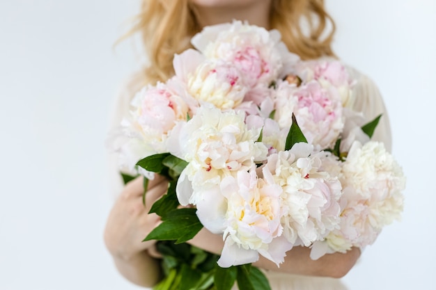 Girl with pink peonies bouquet at white wall