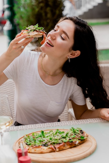 Girl with pinsa romana in cafe on summer terrace. Young woman eating pinsa and drinking wine.