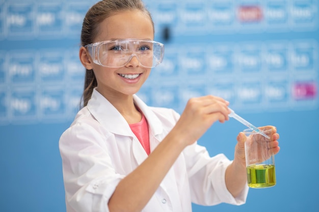 Girl with pipette over glass looking at camera