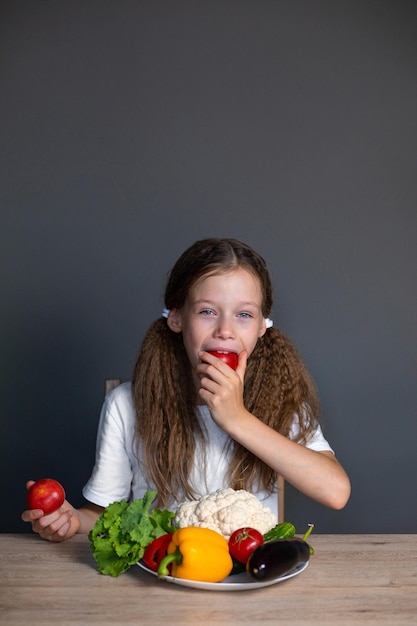 a girl with a plate of fresh vegetables sits at the table and eats tomatoes Healthy eating children