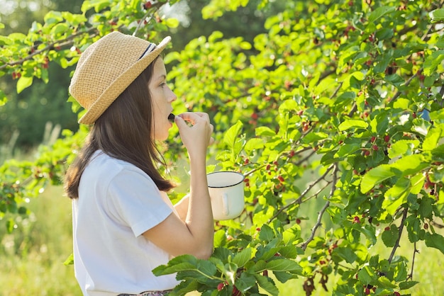 Девушка с удовольствием ест вкусные сладкие спелые ягоды тутового дерева. Летний сезон в саду, натуральные органические ягоды, богатые витаминами, здоровое питание.
