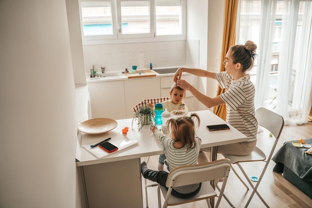 Girl with ponytails reaching for the potted plant while her mother fixing her sister hair during the morning meal