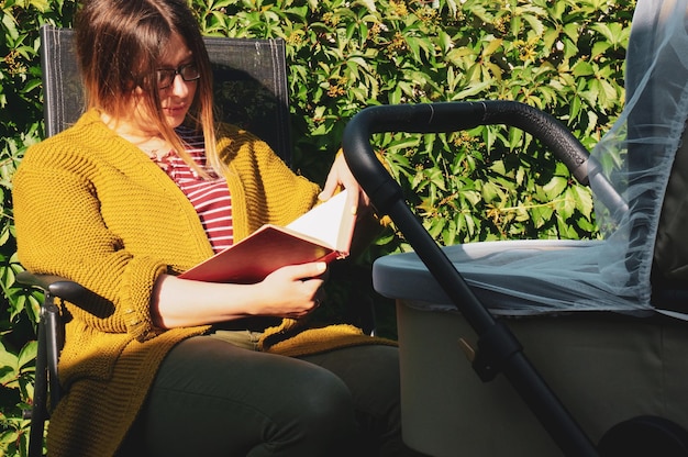 여름 화창한 날에 유모차를 탄 소녀가 자연에서 책을 읽는다