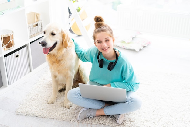 Girl with pretty dog working on laptop in bright room top view