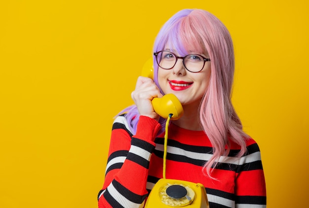 Девушка с фиолетовыми волосами и красным свитером держит телефонный звонок на желтом фоне