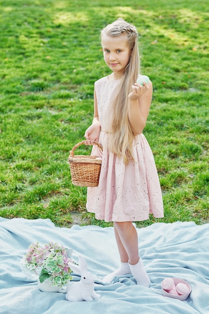 緑の芝生の公園でイースターのウサギと卵を持つ少女