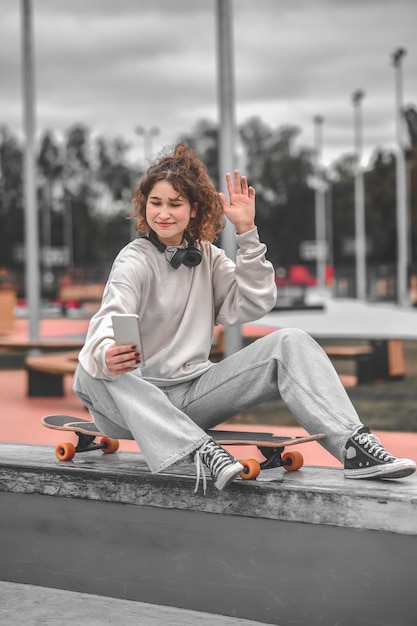 Girl with raised hand sitting on skateboard taking selfie