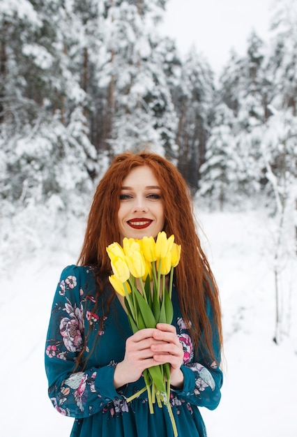A girl with red hair holds a bouquet of yellow tulips on a winter landscape