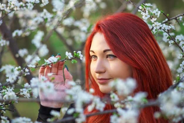 The girl with red hair inhales the fragrance of the flowers of the tree