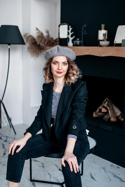 A girl with red lipstick and a beret on her head is sitting in a room on a table