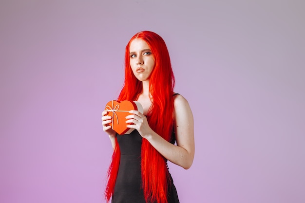 Girl with red long hair holding gift box on pink background