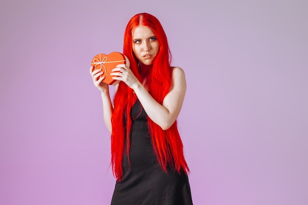 Girl with red long hair holding gift box on pink background