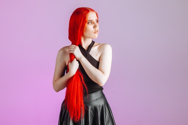 Girl with red long hair and leather skirt posing on pink background