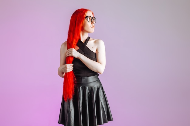 Girl with red long hair and leather skirt posing on pink background