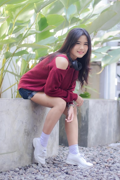 A girl with a red sweater and headphones sits on a concrete wall