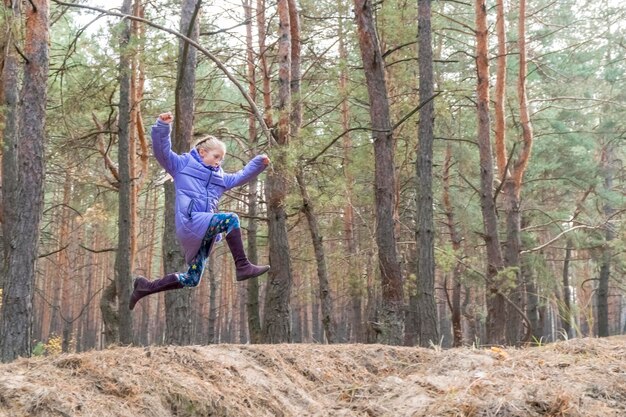 girl with the run jumps over a hole in the pine forest