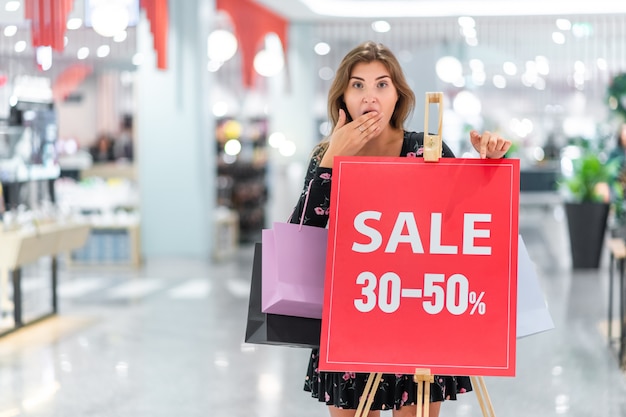 A girl with shopping bags in her hands poses near the red stand