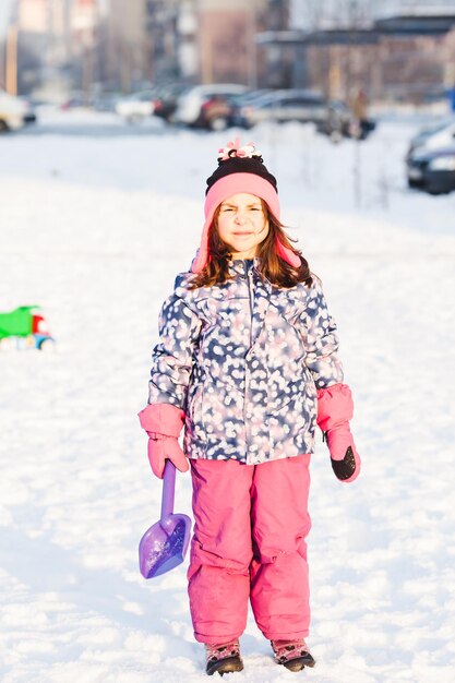 Ragazza con la pala che cammina sulla neve nel parco invernale