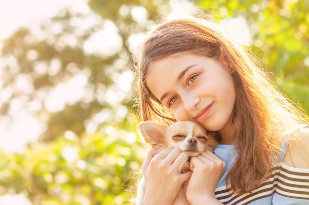 晴れた夏の日に小さな犬を持つ少女。チワワ犬と幸せな10代の少女の肖像画。