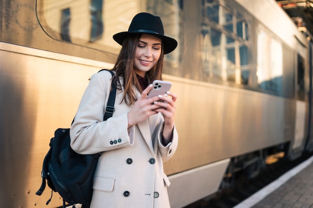 Ragazza con lo smartphone in mano alla stazione ferroviaria.