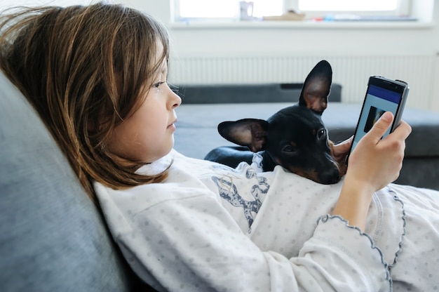 Девушка со смартфоном смотрит на экран. Рядом с ней собака.