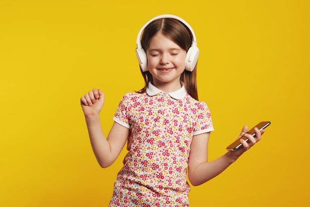 Girl with smartphone and white headphones listening music and dancing