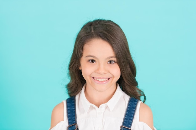 Girl with smile on young face skin on blue background. Girl with long healthy brunette hair, hairstyle.