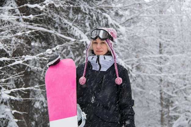 山と降雪の森でスノーボードを持つ少女