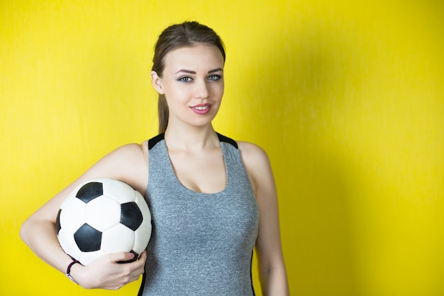 Foto ragazza con un pallone da calcio su giallo.