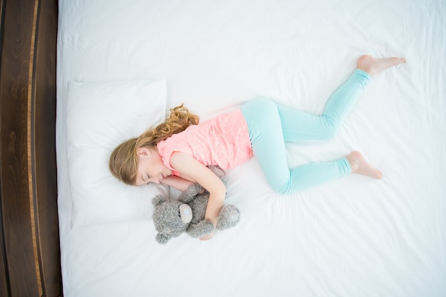 The girl with a soft toy sleeping on the bed. view from above