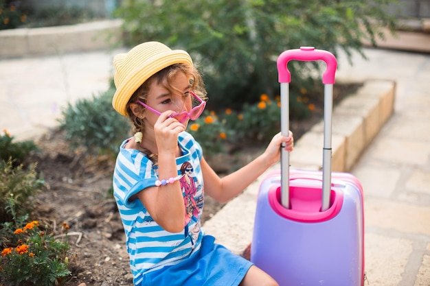 Una ragazza con una valigia un cappello e occhiali da sole sta andando in vacanza aspettando l'arrivo del viaggio nel luogo di residenza in hotel